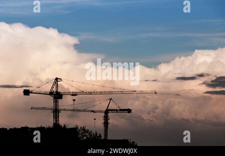 Construction cranes silhouette against the sky with big clouds. Stock Photo