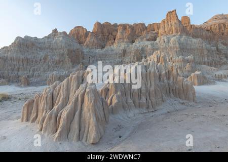 Small rock formation stands in front of large red and yellow rock face in Cathedral Gorge State Park. Stock Photo