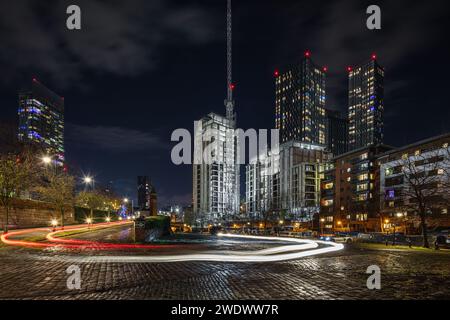 Image on a cobbled Castlefield car park at night in Manchester city centre, UK with car light trails, Beetham Tower, Castle Wharf & Deansgate Square Stock Photo