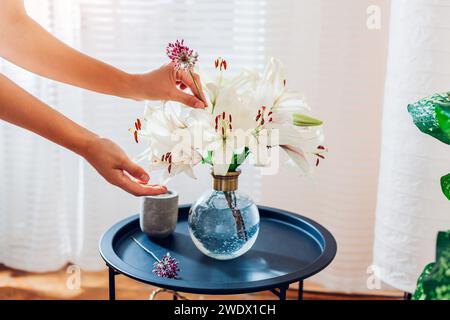 Woman arranges bouquet of roses flowers in transparent vase on table. Taking care of interior and summer decor at home. Close up Stock Photo