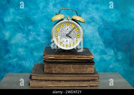 Retro alarm clock and old books on a blue background. Time concept Stock Photo