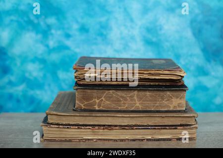 Stack of old books on a wooden table with blue wall background. Stock Photo