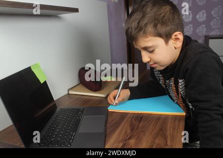 Distance learning online education. Schoolboy boy studies at home and does school homework. Bored student trying to write composition. Stay at home. Stock Photo