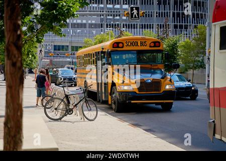 A yellow old school bus drives through the modern city of Calgary. Calgary, Alberta - 06.29.2023 Stock Photo