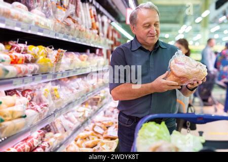 Elderly man chooses chicken meat in supermarket Stock Photo