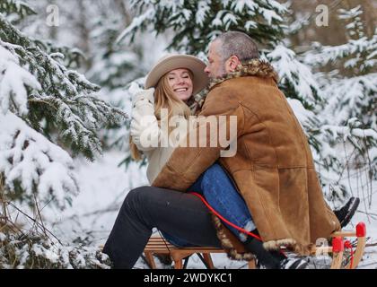 couple in love having fun spending winter time, sitting and hugging on sled Stock Photo