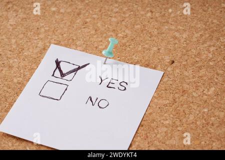 Office cork board with attached piece of paper with words yes or no. Stock Photo
