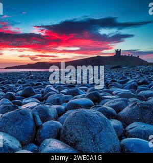 Sunrise at Dunstanburgh Castle in Northumberland looking towards Craster with rocks in foreground and a lovely sunrise in the sky Stock Photo