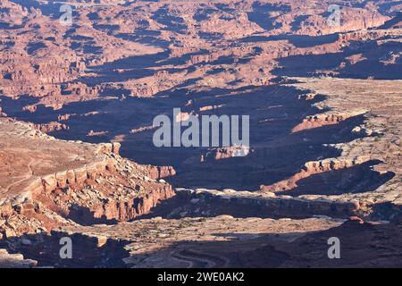 Shadows dance across the canyon floor, where erosion has sculpted the barren rock surface. Stock Photo