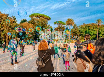 Children play and try to catch the soap bubbles while the adults take photos of them, at Terrazza del Pincio, Rome, Italy. Stock Photo