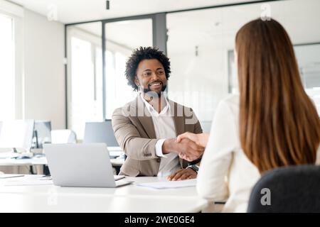 A warm handshake between a man and a woman in a contemporary office setting portrays a friendly agreement or greeting in the corporate world Stock Photo