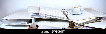 Messy office desk full of ring binders and a coffee cup, wide panoramic format, business concept for stress and overload at work, copy space, selected Stock Photo