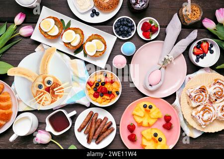 Fun Easter breakfast or brunch table scene. Top down view on a dark wood background. Bunny pancake, egg nests, chick fruit and assorted spring food it Stock Photo