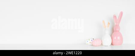 Easter decor on a white shelf. Eggs and modern glass bunnies against a white wall banner. Copy space. Stock Photo