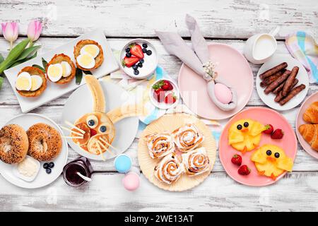 Easter breakfast or brunch table scene. Above view on a white wood background. Bunny pancake, egg nests, chick fruit and a variety of spring food item Stock Photo