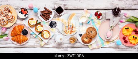 Easter breakfast or brunch table scene. Overhead view on a white wood banner background. Bunny pancake, egg nests, chick fruit and an assortment of sp Stock Photo