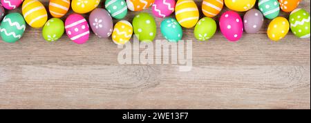 Colorful Easter egg top border. Overhead view on a light wood banner background. Copy space. Stock Photo