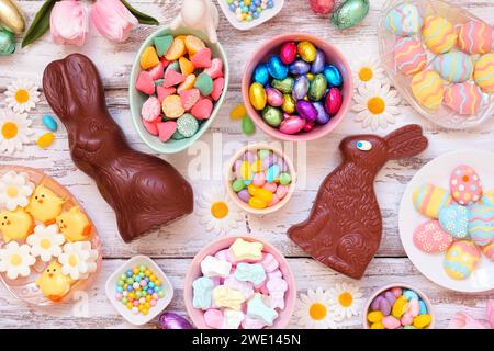 Easter candy table scene. Overhead view over a white wood background. Chocolate bunnies, candy eggs and a variety of sweets. Stock Photo
