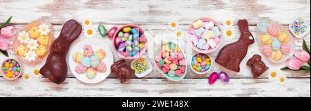 Easter candy table scene. Above view over a white wood banner background. Chocolate bunnies, candy eggs and assorted sweets. Stock Photo