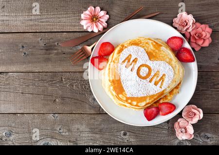 Pancakes with heart shape and MOM letters. Mothers Day breakfast concept. Top view on a rustic wood background. Stock Photo