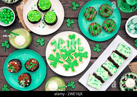St Patricks Day theme desserts. Table scene over a dark wood background. Shamrock cookies, green cupcakes, brownies, donuts and sweets. Above view. Stock Photo
