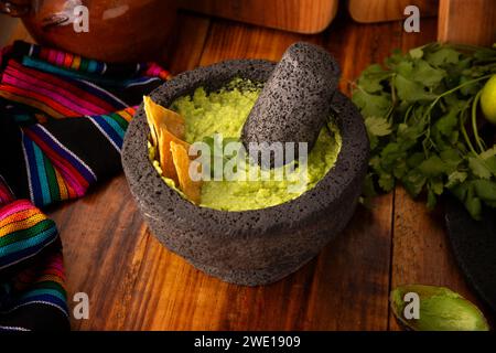 Guacamole. Avocado dip with tortilla chips also called Nachos served in a bowl made with volcanic stone mortar and pestle known as molcajete. Mexican Stock Photo