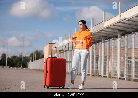 Being late. Worried young woman with red suitcase outdoors Stock Photo