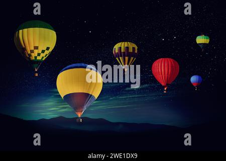Bright hot air balloons flying in starry sky over mountain at night Stock Photo
