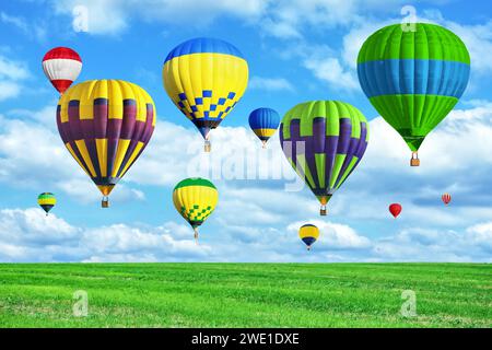 Bright hot air balloons flying in sky with clouds over green meadow Stock Photo