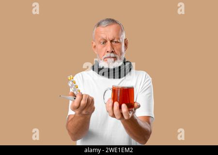 Old man with sore throat holding pills and cup of tea on beige background Stock Photo