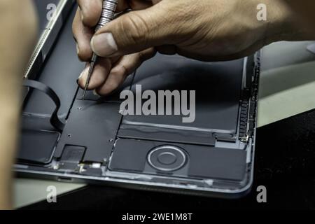 An electronic repair shop technician screwing parts in a tablet repair with his small screws Stock Photo