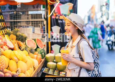 Young Asian woman traveler tourist buying a freshly made juice and walking at outdoor market in Bangkok in Thailand. People traveling, summer vacation and tourism Stock Photo