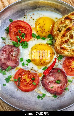 Scrambled eggs with sausage and tomatoes on a wooden background Stock Photo