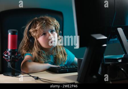 A little boy child uses a desktop at night, a child with computer screen in the room with neon lightning. Portrait of cute child while typing on Stock Photo