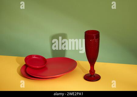 Front view of stacked of round red plates and red glass cup decorated on color background. Blank space for text and design. Contrasting and striking c Stock Photo