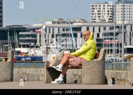 Man and a small dog sitting on a bench out of season at the Gdynia Marina and Port on the Baltic Sea in the resort city of Gdynia, Poland, Europe, EU Stock Photo