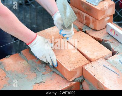 Mason in protective gloves is laying brick wall of a house construction using mortar, trowel and level line, string and spirit level. Stock Photo