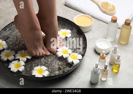 Woman soaking her feet in bowl with water and flowers on light grey floor, closeup. Spa treatment Stock Photo