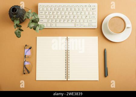 Desktop with blank notepad, keyboard, glasses and coffee cup on brown table. Top view, flat lay. Stock Photo