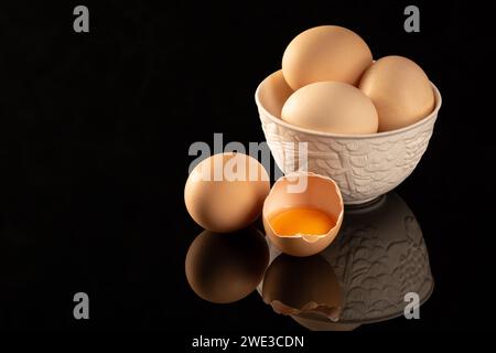 A group of raw, uncooked brown chicken eggs are neatly arranged on a shiny, black reflective surface, creating an ideal setup for engaging food photog Stock Photo