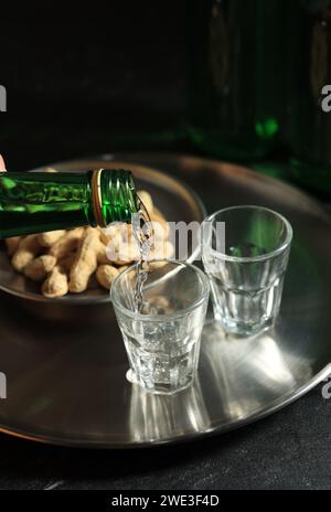 Pouring Soju or Mineral Water to Small Glass Cup. Alcoholic Clear Distilled Korean Soju. Stock Photo