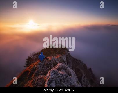 Man  on rock above valley within daybreak and watch to hot Sun. Beautiful moment the miracle of nature Stock Photo