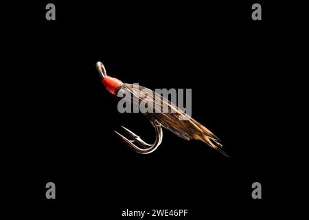Macro shot colorful fishing fly isolated on a black background. Hand made fly fishing flies. Fluffy fly fishing hook isolated. Stock Photo