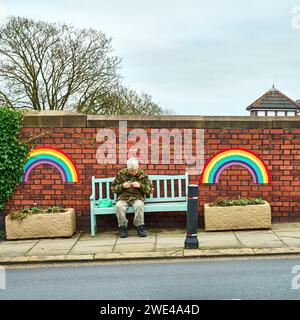 Man sat on street bench between rainbows connected to brick wall Stock Photo