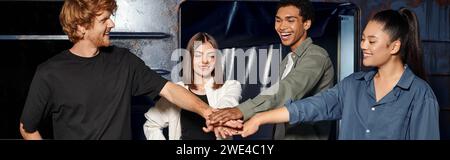 young multicultural group of friends stacking hands while having quest in escape room, banner Stock Photo