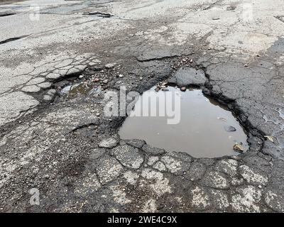 Pit with puddle on the asphalt road cover. Close-up shot. Stock Photo