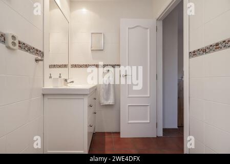 Small modern design bathroom with white wooden furniture with porcelain sink, terracotta flooring and white wooden framed mirror Stock Photo