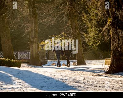 Couple wearing warm winter clothes walking through a snow covered Pavilion Park in Buxton on a sunny winter day. Stock Photo