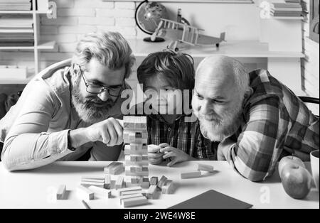 Grandfather father and pupil son smiling against home background. Happy generational muti three generation men family portrait. Jenga game at home. Stock Photo