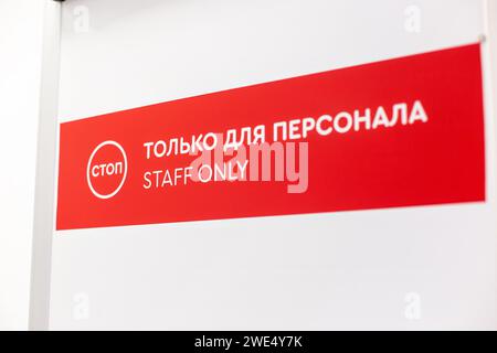 Red and white 'Staff Only' sign with bilingual text in English and Russian above door Stock Photo